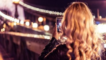 Blondes Mädchen fotografiert in der Nacht mit ihrem Smartphone eine erleuchtete Brücke