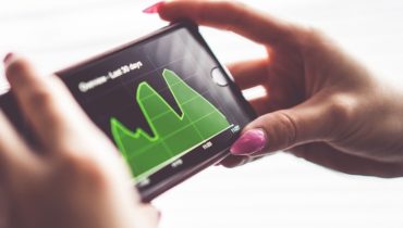 Frauenhänge halten ein Smartphone in der Hand auf dem eine Grafik zu sehen ist.