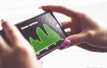 Frauenhänge halten ein Smartphone in der Hand auf dem eine Grafik zu sehen ist.