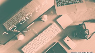 Computerbildschirm, Tastatur, Maus, Laptop und Kamera auf einem Schreibtisch