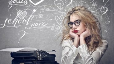 Blonde Frau mit zerstausten Haaren schaut auf eine alte Schreibmaschine und hat viele Gedanken im Kopf, die um sie herum schwirren.