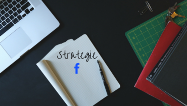 Ein Laptop liegt mit einem aufgeschlagenen Notizbuch und einem Stift auf einem Tisch. In dem Notizbuch steht das Wort Strategie und darunter ist das blaue F von facebook zu sehen.