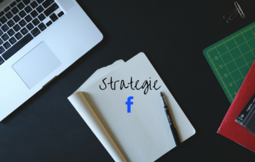 Ein Laptop liegt mit einem aufgeschlagenen Notizbuch und einem Stift auf einem Tisch. In dem Notizbuch steht das Wort Strategie und darunter ist das blaue F von facebook zu sehen.