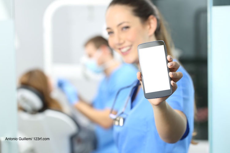 Zahnarzthelferin in einer blauen Uniform hält ein Smartphone in ihrer Hand nach vorne in die Kamera