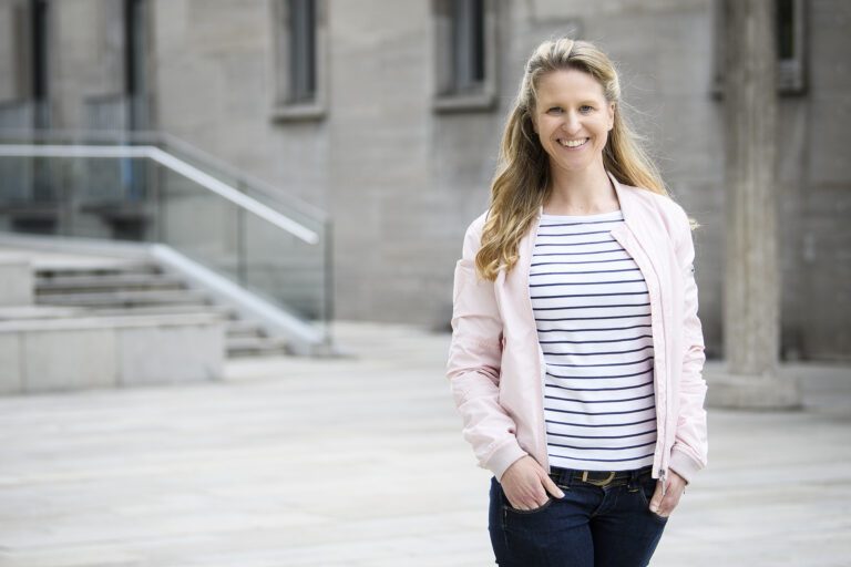 Daniela Sprung steht vor einem Gebäude mit einer Treppe.